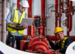 Técnicos realizando inspección y registro de mantenimiento en un sistema contra incendio industrial con bombas y tuberías